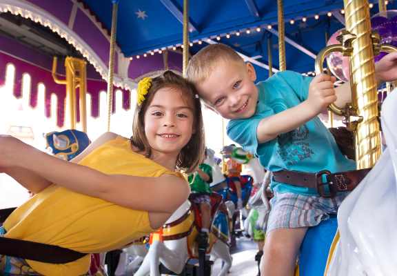 a brother and sister enjoy the merry go round at a theme park in florida